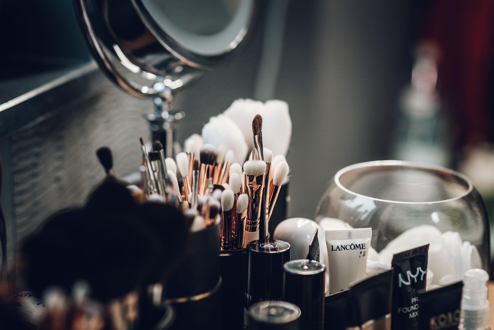 Professional makeup brush set organized on a vanity table with beauty products, cotton pads, and a mirror, creating an elegant makeup station.